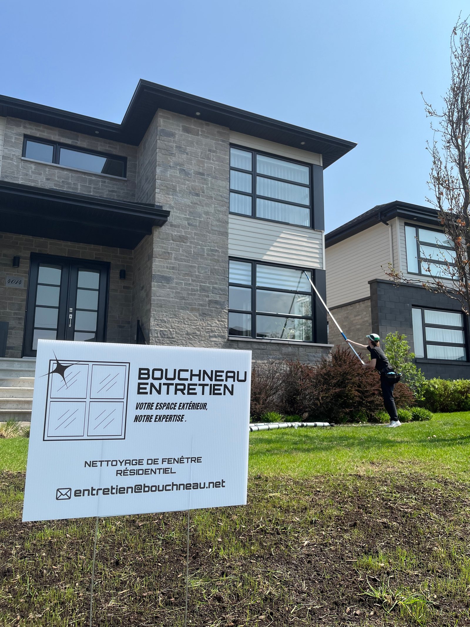 Technicien de Bouchneau Entretien lavant les fenêtres d’une résidence devant une affiche de l’entreprise