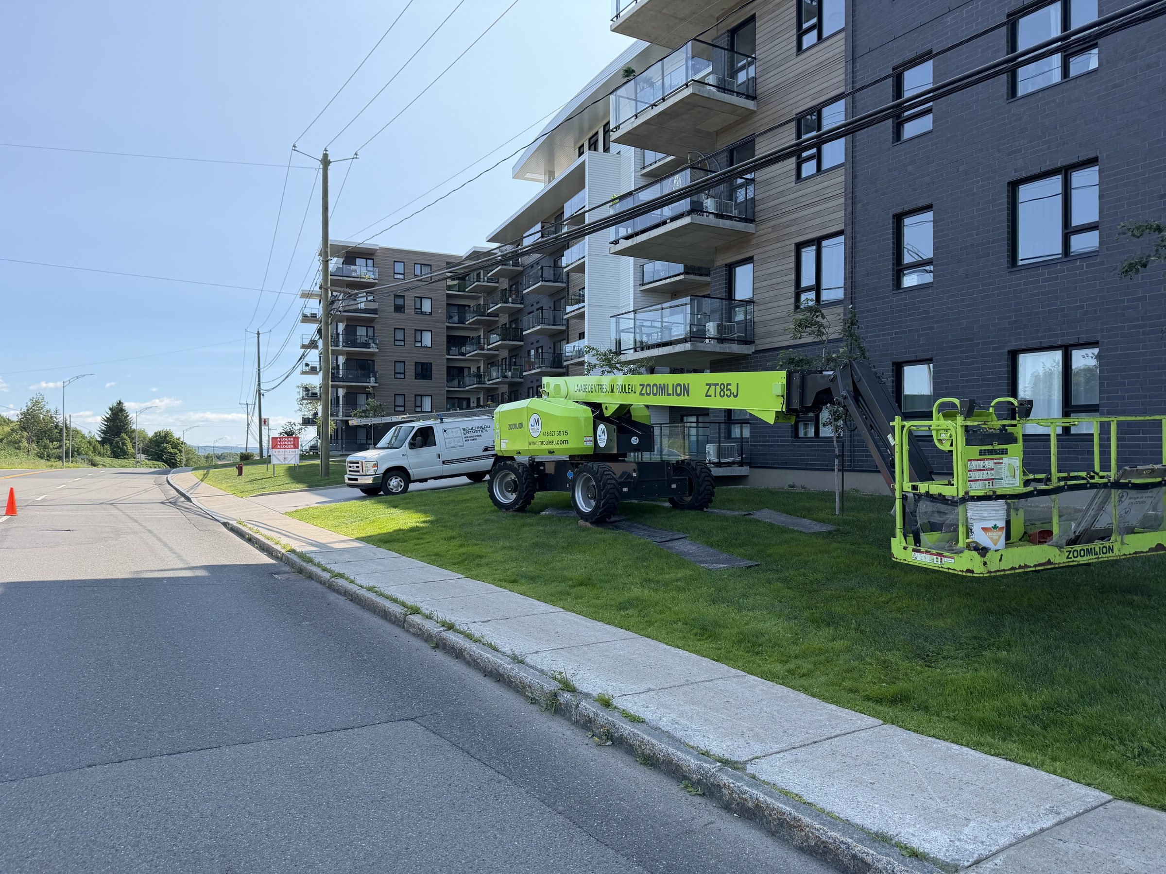 Nacelle élévatrice et véhicule de service déployés devant un immeuble multilogement
